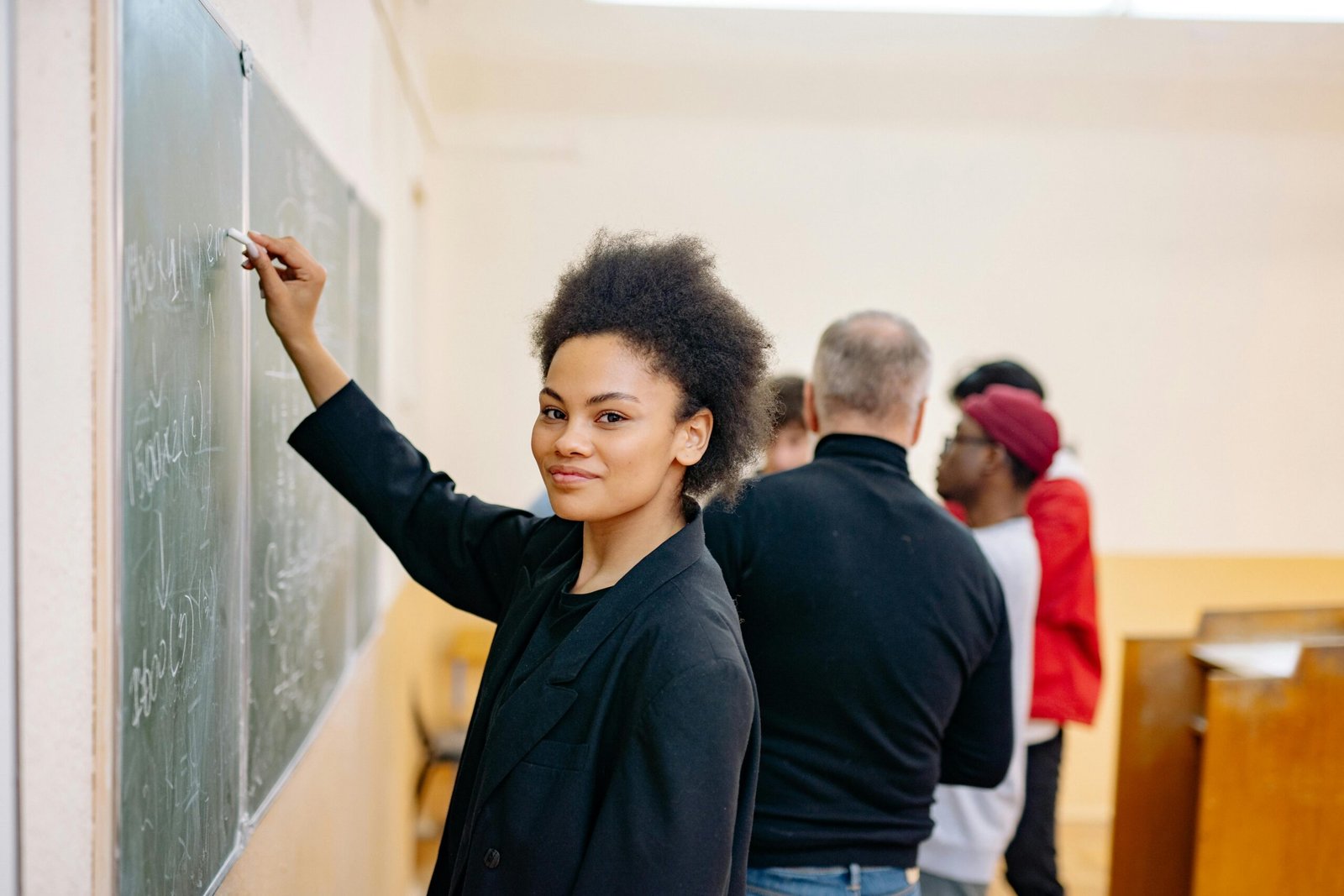 A student writing confidently on a blackboard in a lively classroom setting with peers.