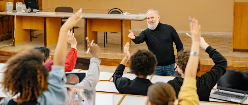 pexels-photo-8199166-8199166 Professor engaging with students in a lively university classroom discussion as students raise hands.